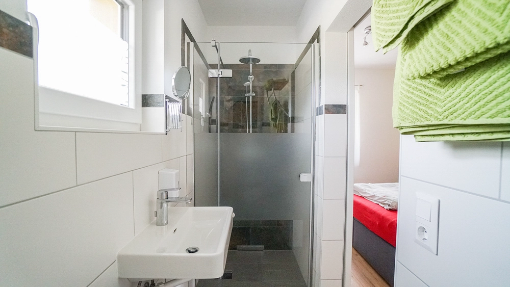 „Hahns Herberge“ – Kleines Badezimmer mit Blick in ein Schlafzimmer Interiorfotografie eines Raums mit wohnlicher Atmosphäre.